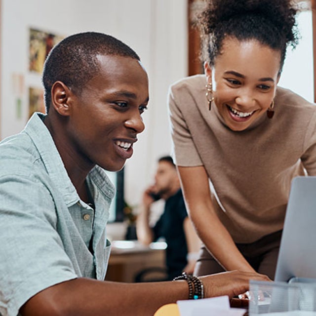 Man and woman collaborating on a laptop in a busy office