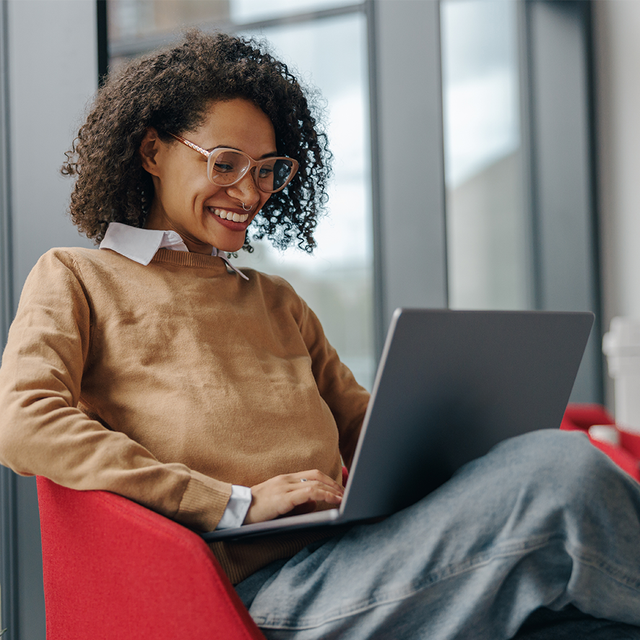 Woman sitting in a chair in an office, smiling at her laptop