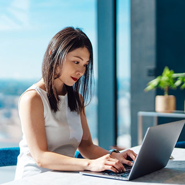 Woman in front of high-rise window working on a laptop