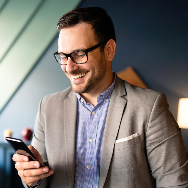 Man in a bright office smiling at a phone in his hand