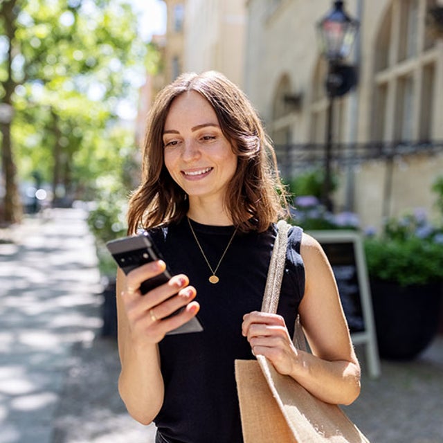 Smiling woman outdoors looking at smartphone in hand