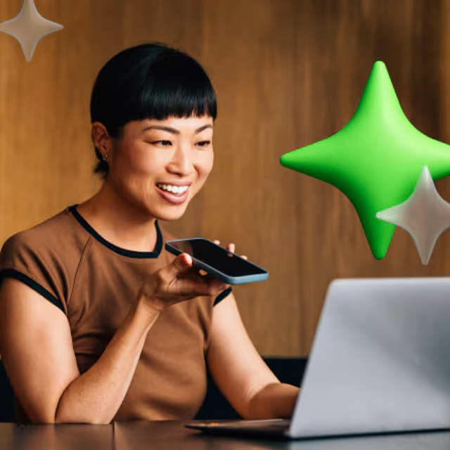 Woman at a desk talking into a phone while working on a laptop