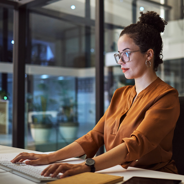 Woman wearing glasses typing on a desktop computer