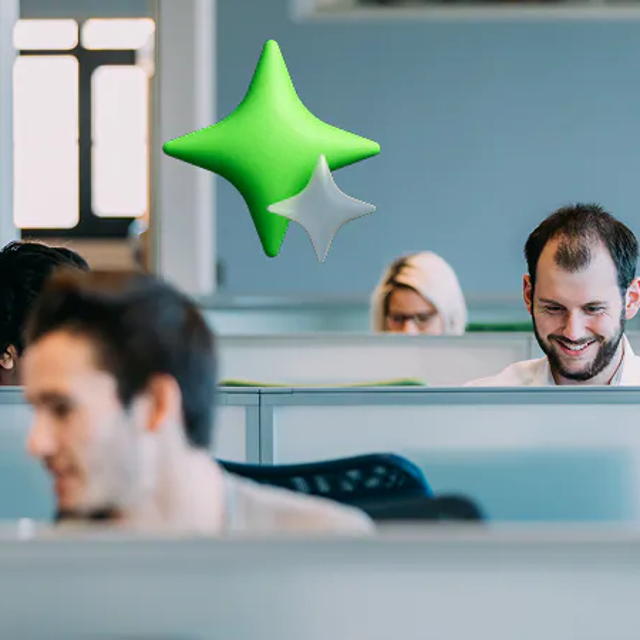 Employees working in cubicles with a four-pronged green star overhead to indicate AI