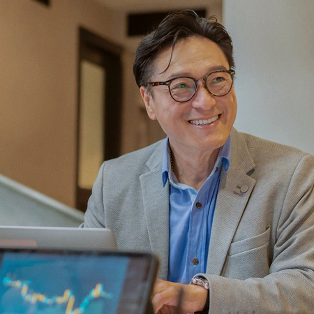 Smiling man in glasses with a laptop showing a financial chart in the foreground