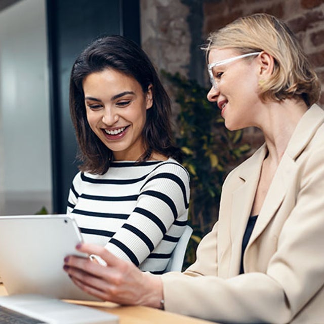 2 women looking at a tablet in front of open laptops