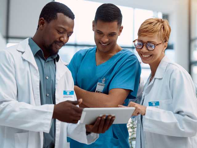 Group of hospital workers looking at a tablet while standing in a hallway