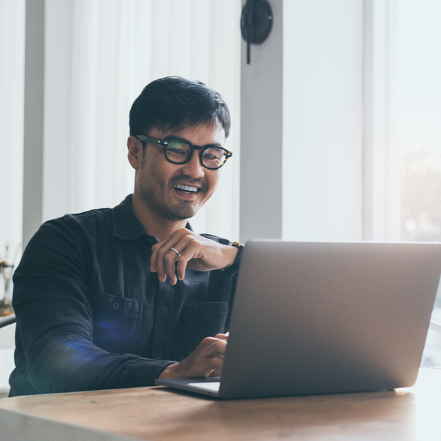 Man sitting at a desk smiling at a laptop in a bright office