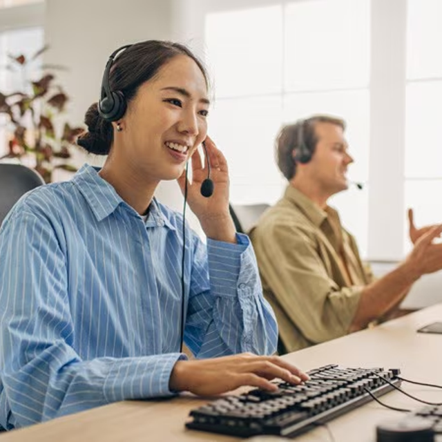 Woman and man wearing headsets working on computers in a bright office