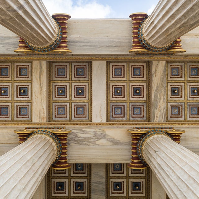 Camera shot from the ground looking up four pillars to an architected ceiling