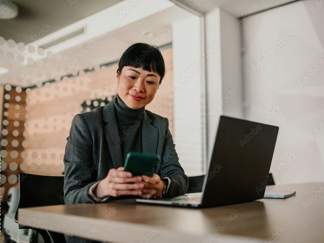 Tech leader looking at her phone in front of an open laptop on a desk