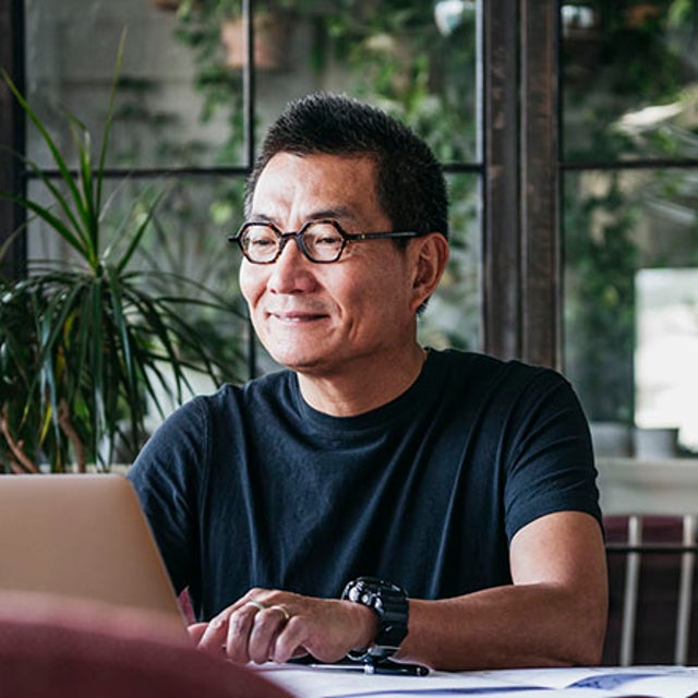 Man working on a laptop at a desk surrounded by green plants