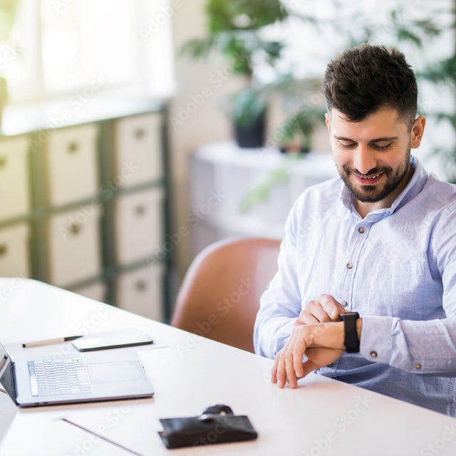 Man at desk in bright office looking at his watch