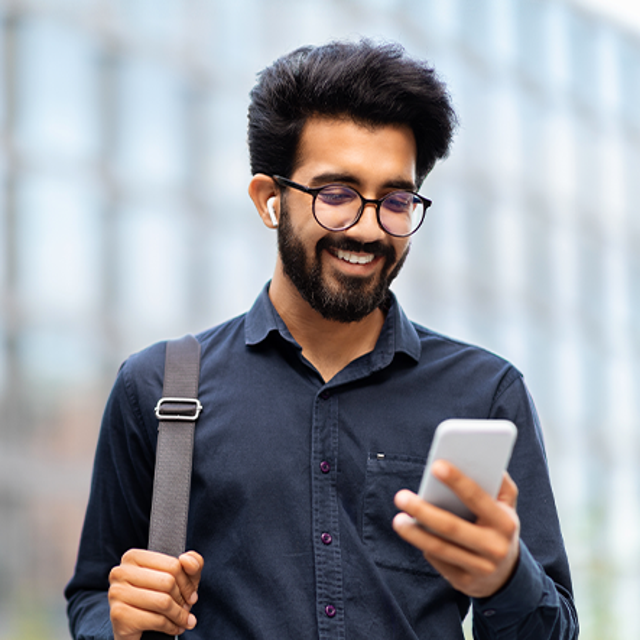Man holding and smiling at phone in front of a tall building
