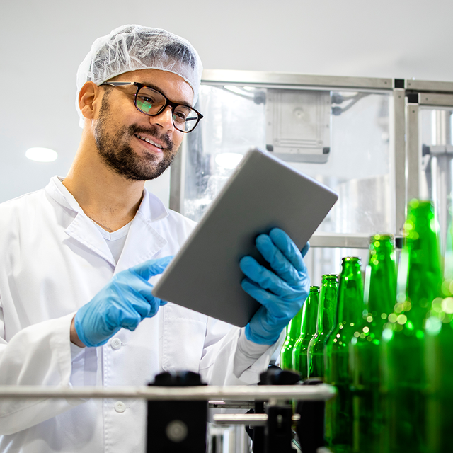 Preventive maintenance: employee at a bottling plant smiling at a tablet in his hands