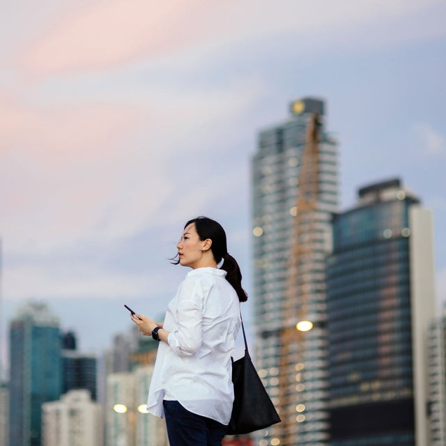 Woman walking outdoors with a phone in her hand and skyscrapers in the background