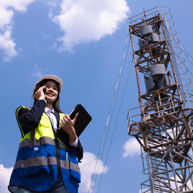 Female telecom worker talking on a phone near a cell tower