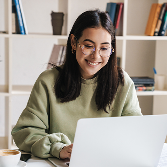Woman smiling and typing on a laptop in front of a bookcase