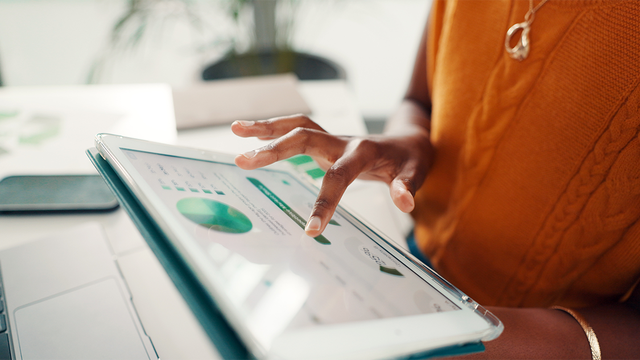 A hand on a tablet displaying graphs