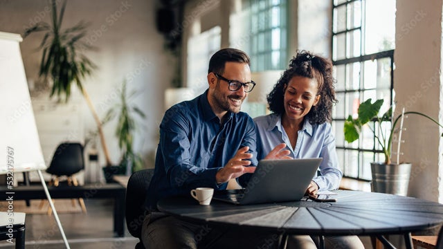 Two workers collaborating in front of an open laptop in a bright office