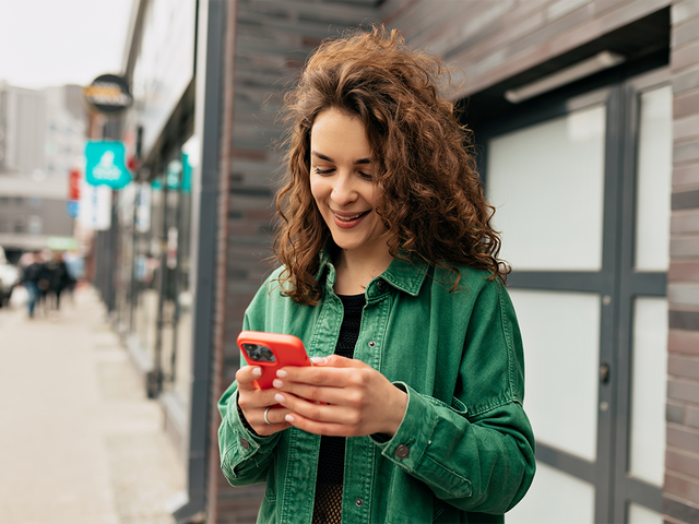 Woman standing outside a downtown shop smiling at the phone in her hands