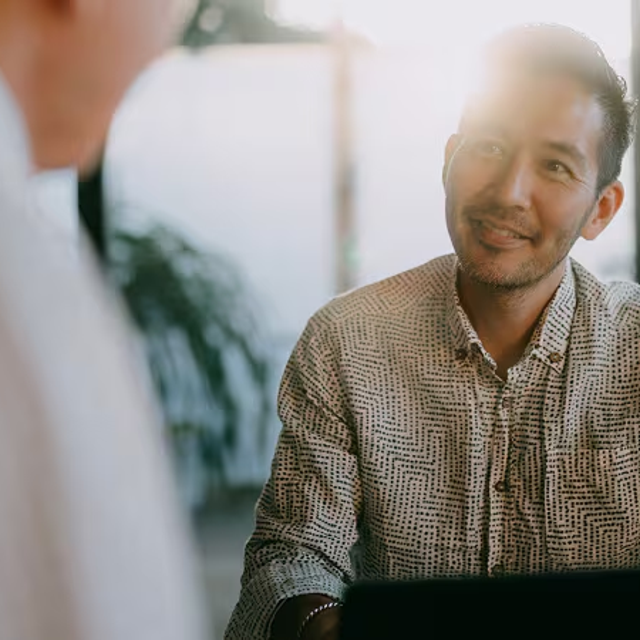 Man with an open laptop looking up at a co-worker in a bright office