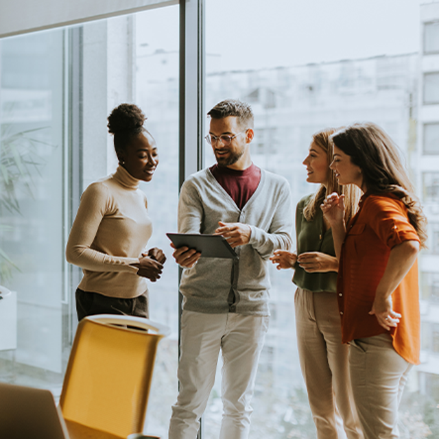 Co-workers standing in front of a window around a tablet in an office