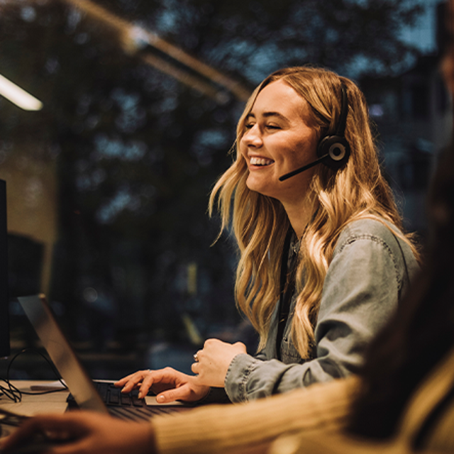 Woman wearing a headset smiling at computer monitors