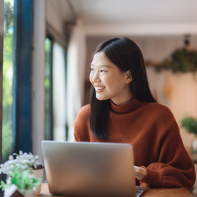 Woman at an open laptop smiling as she looks out a window