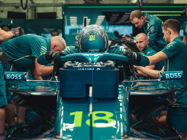 View from the front of Aston Martin Aramco Formula One racecar while employees work on it