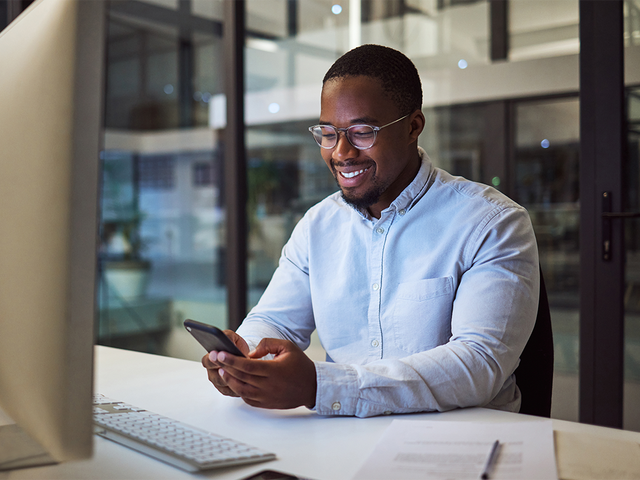 Man working on phone in his hands in front of computer on desk