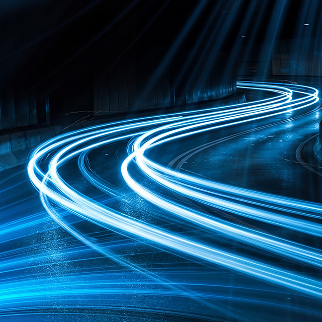 Long exposure photograph capturing vibrant blue light streaks making sharp turns on a dark wet road