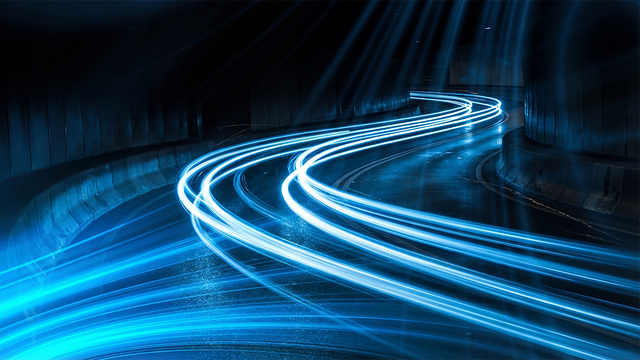 Long exposure photograph capturing vibrant blue light streaks making sharp turns on a dark wet road