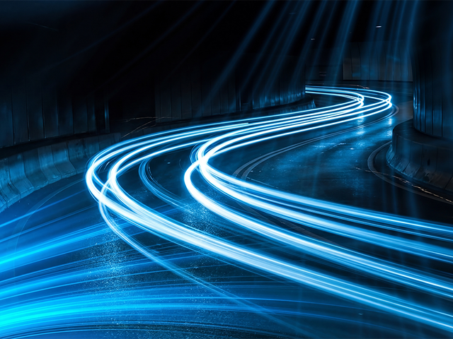 Long exposure photograph capturing vibrant blue light streaks making sharp turns on a dark wet road