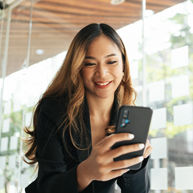 Woman in a bright office smiling at the phone in her hand