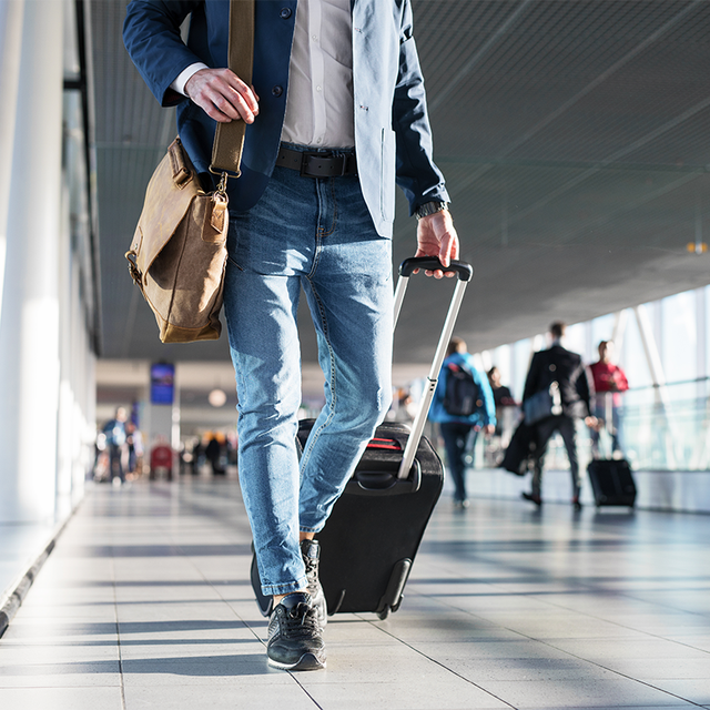 Man with shoulder bag and hand luggage walking in airport terminal