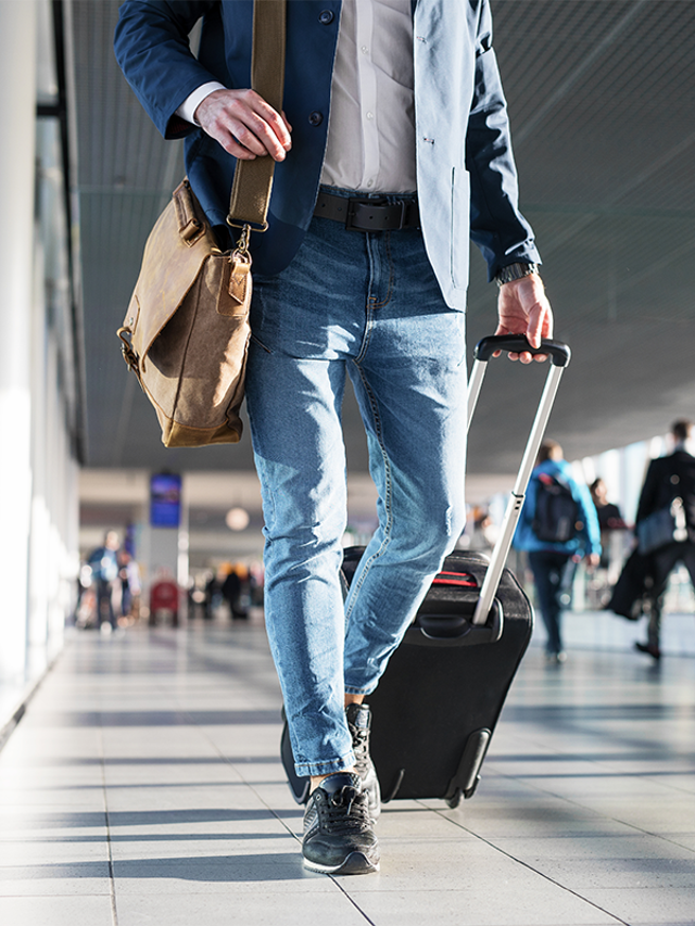 Man with shoulder bag and hand luggage walking in airport terminal