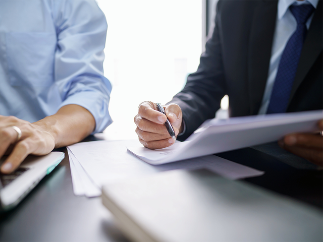 Legal counsel presenting paperwork to someone working on a laptop
