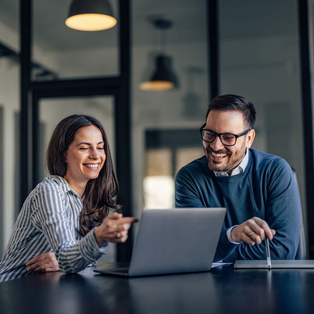 Two workers smiling at an open laptop on a conference room table