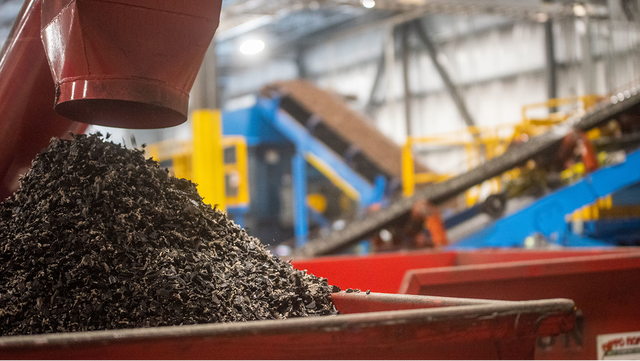 A close-up of shredded tire material pouring into a red container on the recycling facility floor.