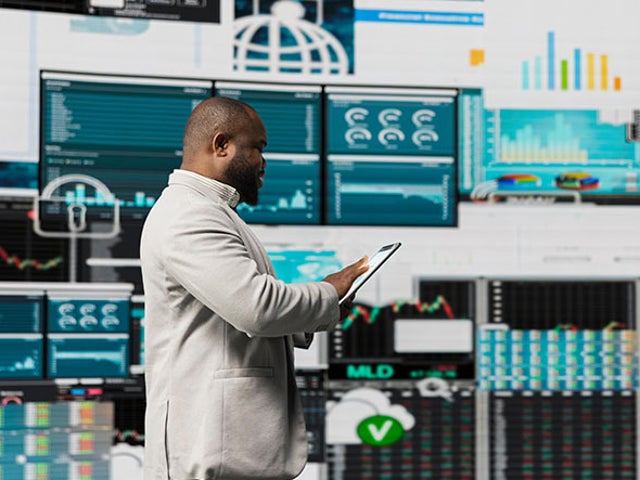 Man looking at a tablet in his hands in front of a wall of financial reports