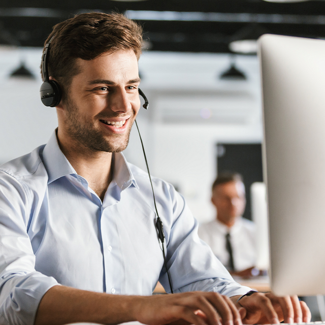 Man wearing a headset smiling at a computer monitor 