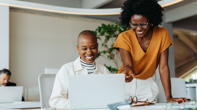 Seated woman and standing woman collaborating on a laptop in an office