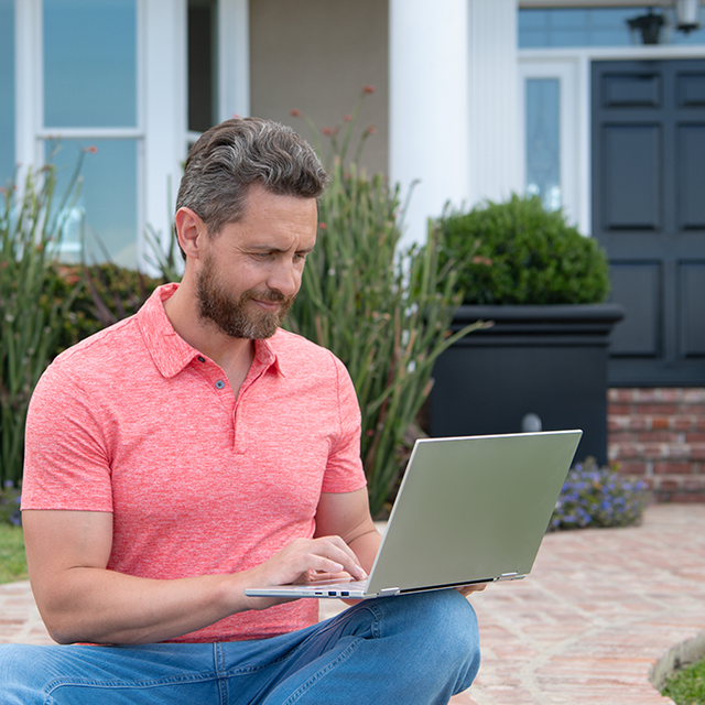 Man sitting on steps outside his house working on laptop