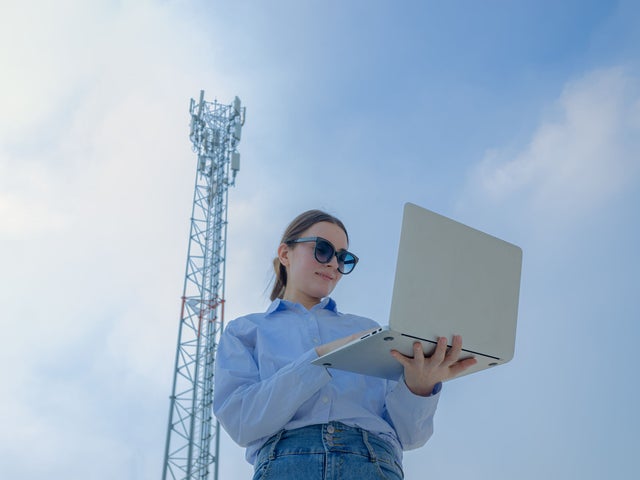 Woman holding a laptop in front of a telecommunication tower