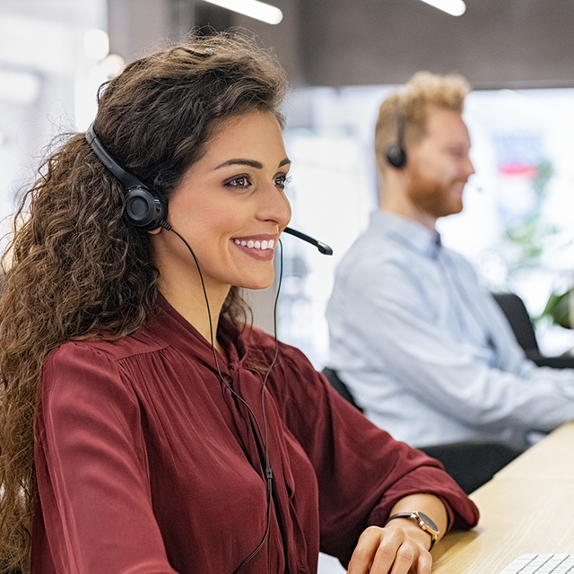 Three workers in a call center wearing headsets and smiling at computer screens