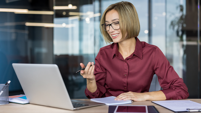 Woman at a desk holding a pen pointing at her open laptop