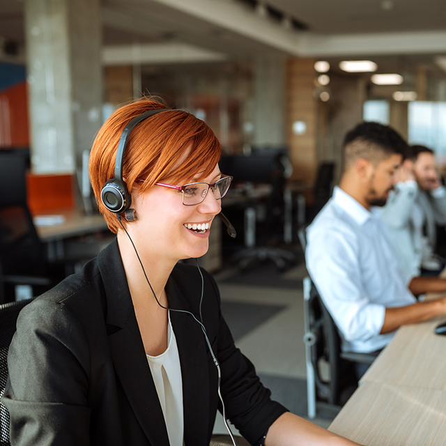 Woman wearing a headset working in a call center with a line of other agents in the background