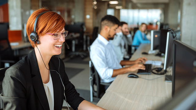 Woman wearing a headset working in a call center with a line of other agents in the background