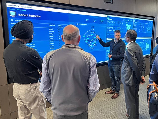 Four businessmen gathered around a life-size display of the CEO Dashboard